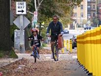 Bicycle Program - an adult riding a bike alongside a child on a training-bike in a bike lane